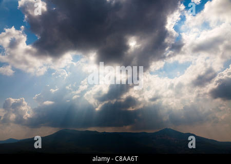 Rotture di pioggia nuvole con il cielo blu e sun streaming attraverso le nuvole e colline Foto Stock