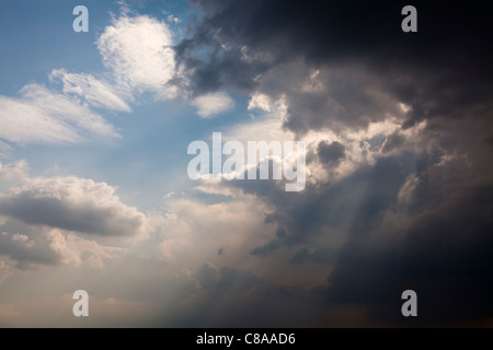 Rotture di pioggia nuvole con il cielo blu e sun streaming attraverso le nuvole e colline Foto Stock