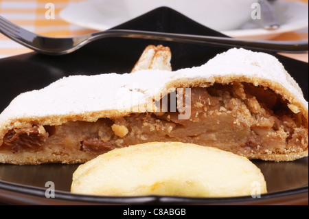 Strudel di mele (Apfelstrudel) servita su una piastra nera con una tazza di tè in background. Foto Stock