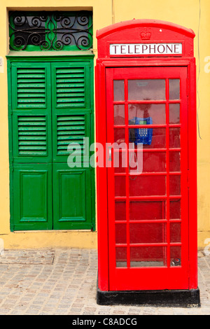 Un tradizionale rosso telefono in inglese nella parte anteriore della parete gialla e una porta verde, Malta Foto Stock