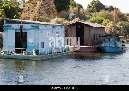 Fiume Nilo banca con piccolo blu, individuato incanalati barca ormeggiata lungo capannone, floating stazione pompa in primo piano Foto Stock