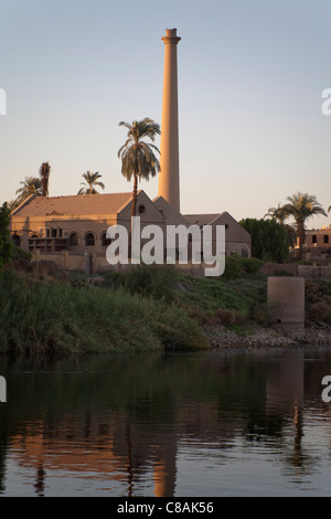 Una sezione del fiume Nilo banca con camini industriali e le palme si riflette nell'acqua ancora, Egitto, Africa Foto Stock