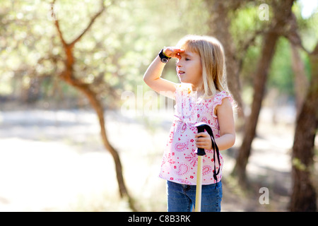 Escursionismo kid ragazza in cerca la mano in testa nella foresta per esterno Foto Stock