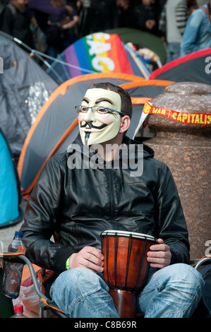 Occupare Londra davanti a San Paolo. Parte di protesta in tutto il mondo . Protester con tamburo indossando maschera di Guy Fawkes di fronte di tende Foto Stock