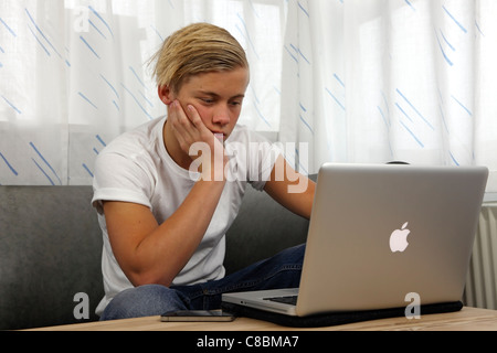 Adolescente usando il suo MacBook Pro Apple per i compiti a casa mantenendo i suoi amici aggiornati su online i servizi di social networking Foto Stock