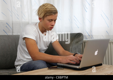 Adolescente di sesso maschile con il suo MacBook Pro Apple per i compiti a casa mantenendo i suoi amici aggiornati su social media. L'iPhone non lontano. Foto Stock