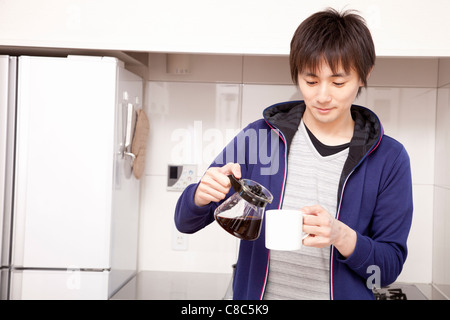 Giovane uomo versando il caffè da server a mug Foto Stock