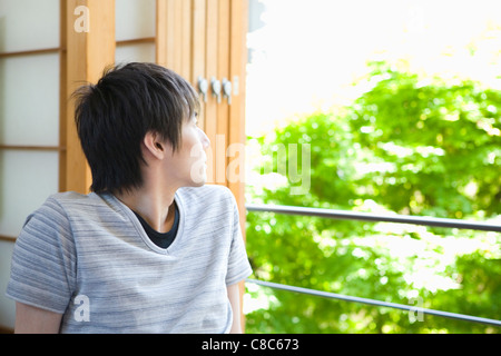Giovane uomo che guarda lontano dalla finestra Foto Stock