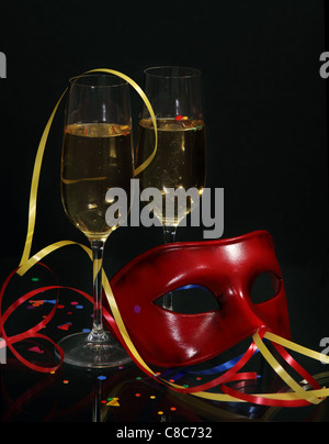 Champagne in due bicchieri con stelle filanti e maschera di Carnevale su sfondo nero Foto Stock