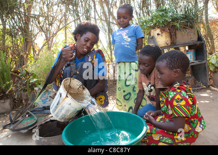 Una donna e i suoi figli attingere acqua da un pozzo in Mongu, Zambia, Sud Africa. Foto Stock