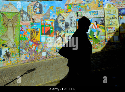 © Tony Bartolomeo una donna cammina passato ta murale raffigurante scene locali sulla scogliera Blands,Scarborough,North Yorkshire Foto Stock