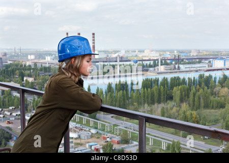 Lavoratore di sesso femminile in fabbrica. In piedi nel casco all'altitudine e guardando verso il basso. Area dello stabilimento su sfondo Foto Stock