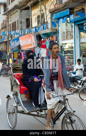 Scena di strada nella città santa di Varanasi, giovane donna musulmana in black burkha giostre in rickshaw, Benares, India settentrionale Foto Stock