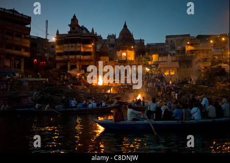 I turisti guardare la cremazione indù sulla pira funeraria a Manikarnika Ghat, Fiume Gange, nella città santa di Varanasi, Benares, India Foto Stock
