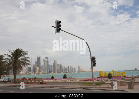 Giovane seduto sulla Corniche con il Qatar Doha skyline della città in background Foto Stock