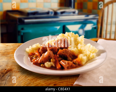 Tradizionale casseruola di agnello brasata e purè di patate serviti su a. piatto su un tavolo di legno in un ambiente di cucina Foto Stock