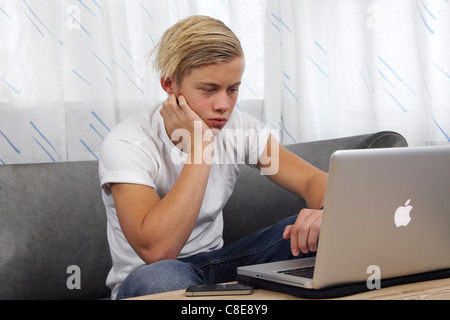 Adolescente di sesso maschile con il suo MacBook Pro Apple per i compiti a casa mantenendo i suoi amici aggiornati sulle reti sociali. GCSE alta scuola Foto Stock