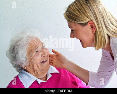 Bionda e giovane badante donna saluta affettuosamente alert notevole ridendo dai capelli bianchi felice senior età 97 anni lady Foto Stock