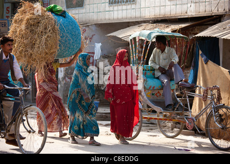 Le donne indiane a piedi in strada, uno portante delle balle di paglia sulla testa, in Nandi vicino a Varanasi, Benares, India settentrionale Foto Stock