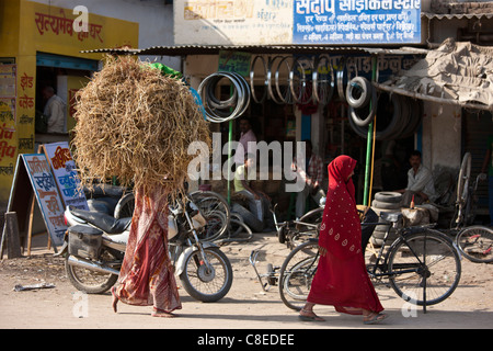 Le donne indiane a piedi in strada, uno portante delle balle di paglia sulla testa, in Nandi vicino a Varanasi, Benares, India settentrionale Foto Stock