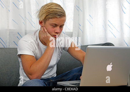 Adolescente maschio su un lettino usando il suo MacBook Pro Apple per i compiti a casa mantenendo i suoi amici aggiornati su le reti sociali Foto Stock