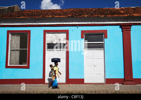 Donna camminare davanti casa colorati, Inhambane, Mozambico Foto Stock