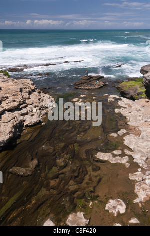 Costa occidentale Portogallo vicino a Lorinho un ruscello pieno di erbacce scende al mare dal bordo della scogliera e un uomo in lontananza pesca a riva su una roccia Foto Stock