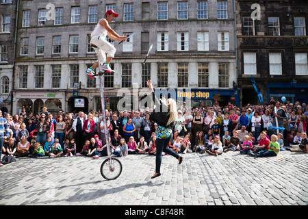 Giocoliere al Festival di Edimburgo su un monociclo ottenendo una donna a lanciare coltelli per lui per la cattura di Foto Stock