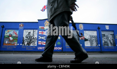 Un uomo cammina passare un murale lealisti nell'streetsof sabbiosa area di riga a Belfast, Irlanda del Nord Foto Stock