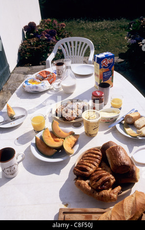 Pendruc, Bretagna, Francia. Tavolo per la prima colazione con la pasticceria, pane, croissant, pain au chocolat, melone, formaggio, succo d'arancia. Foto Stock