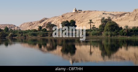 La sezione del fiume Nilo banca con cinque uomini la pesca in una piccola imbarcazione con alberi, una collina con un santuario in cima, e riflesso perfetto Foto Stock