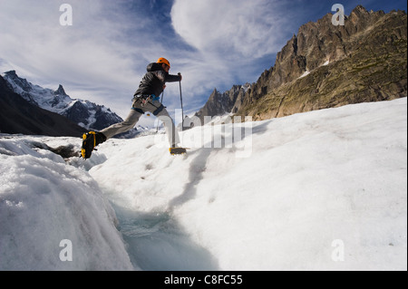 Scalatore di saltare attraverso un flusso di crevase sul Mer de Glace ghiacciaio, Mont Blanc range, Chamonix, sulle Alpi francesi, Francia Foto Stock