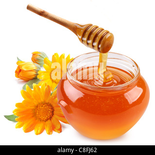 Il miele si riversa con bastoni in un vaso. I fiori sono nelle vicinanze. Isolato su sfondo bianco. Foto Stock