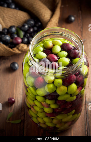 Olive in salamoia (con acqua e con acqua e sale in un barattolo di vetro) su legno Foto Stock