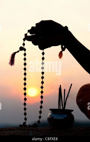 Man mano utilizzando Rudraksha indiano / Japa Mala i grani di preghiera e di incenso . Silhouette