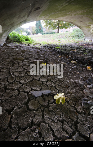 Un fiume secco in autunno mostra incrinato il fango. Il ponte dà un'idea di quanto sia profonda l'acqua dovrebbe essere. Foto Stock