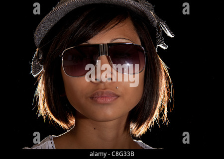 Una immagine illuminata da dietro di una bella ragazza asiatica indossando occhiali da sole. Foto Stock