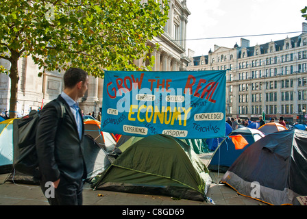 Occupare Londra, St Pauls, in primo piano un grande striscione "crescere l economia reale' essendo letto dal lavoratore della città, più tende. Foto Stock