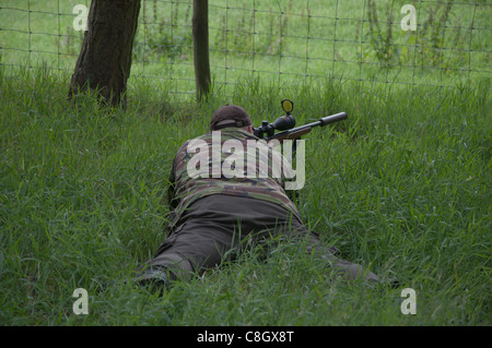 Uomo sdraiato in un'erba lunga con giacca camouflage, guardando e aspettando con un fucile .22 a Weardale, nella contea di Durham Foto Stock