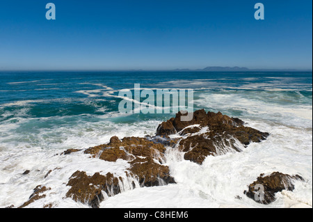 La frantumazione delle onde sui massi lungo il percorso 44 Table Mountain in background in Sud Africa Foto Stock