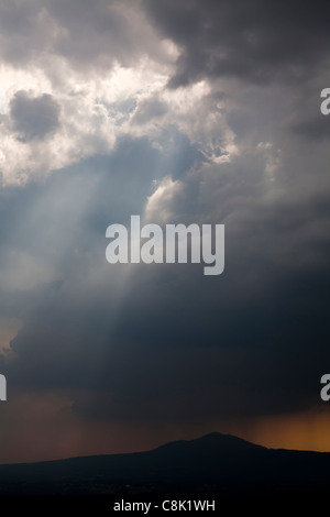 Rotture di pioggia nuvole con il cielo blu e sun streaming attraverso le nuvole e colline e orizzonte giallo Foto Stock