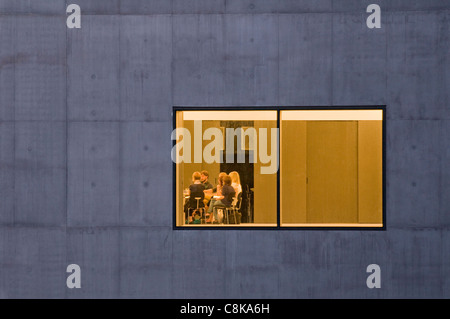Vista attraverso la finestra di vetro (bagliore dorato di luci e persone seduti, incontro al tavolo all'interno) - Hepworth Gallery, Wakefield, West Yorkshire, Inghilterra, Regno Unito Foto Stock