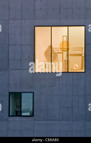 Vista attraverso la grande finestra della Galleria Hepworth, luci accese (bagliore dorato) e pezzi scultorei esposti all'interno - Wakefield, West Yorkshire, Inghilterra, Regno Unito. Foto Stock