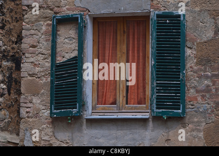 Fatiscenti persiane verdi crollando su una finestra di rosso-arancio tende a Chianciano Terme, Umbria, Italia. Foto Stock