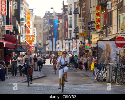 Donna Bicicletta Equitazione e guardando il suo cellulare, Damstraat, Amsterdam, Paesi Bassi Foto Stock