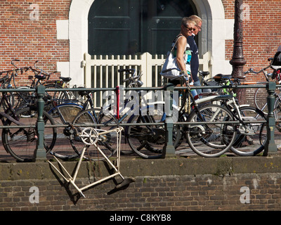 Relitto di bicicletta ancora incatenato ad una ringhiera sul canale ad Amsterdam in Olanda con persone di passaggio Foto Stock