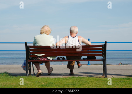 Coppia di anziani seduti su un banco che guarda al mare sulla giornata di sole a Seaton Carew vicino a Hartlepool, England, Regno Unito Foto Stock