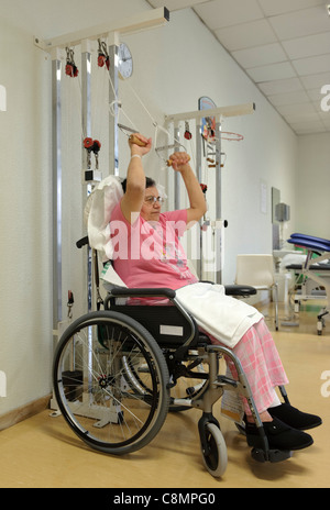 Una donna su una sedia a rotelle facendo esercizi di riabilitazione fisica in ospedale è la fisioterapia palestra Foto Stock