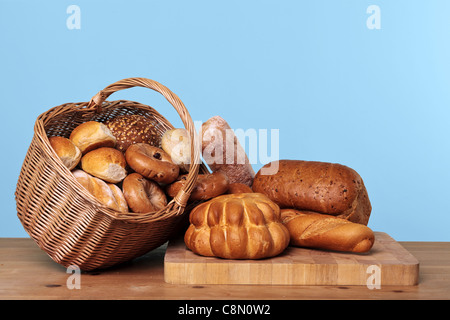 Foto di vari tipi di forme di pane e panini in un cesto di vimini su un tavolo di legno con sfondo blu. Foto Stock