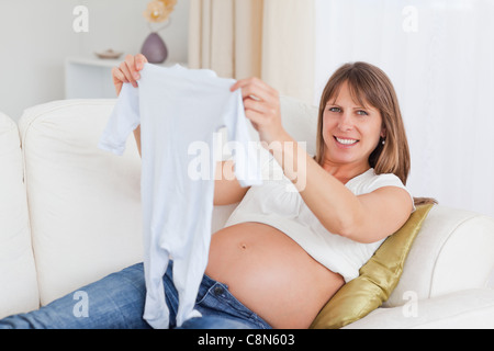 Incantevole donna incinta tenendo un bambino crescere mentre giaceva su un divano Foto Stock